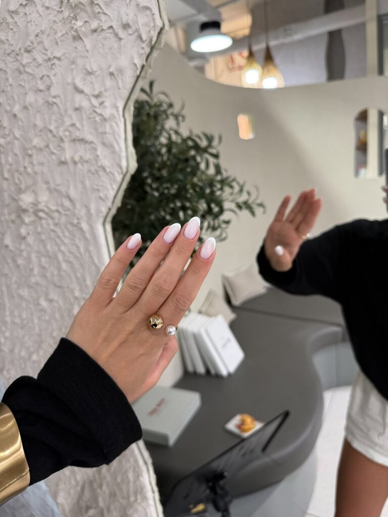 Mão de pele clara, com anel dourado e unha amendoada branca
