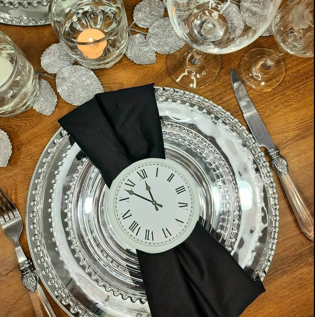 Mesa posta com sousplat e prato na cor prata, guardanapo preto com relógio desenhado
