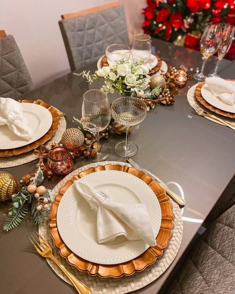 Mesa cinza decorada para o Ano-Novo, com sousplats brancos e dourados, arranjo com flores brancas e bolas de Natal no centro da composição