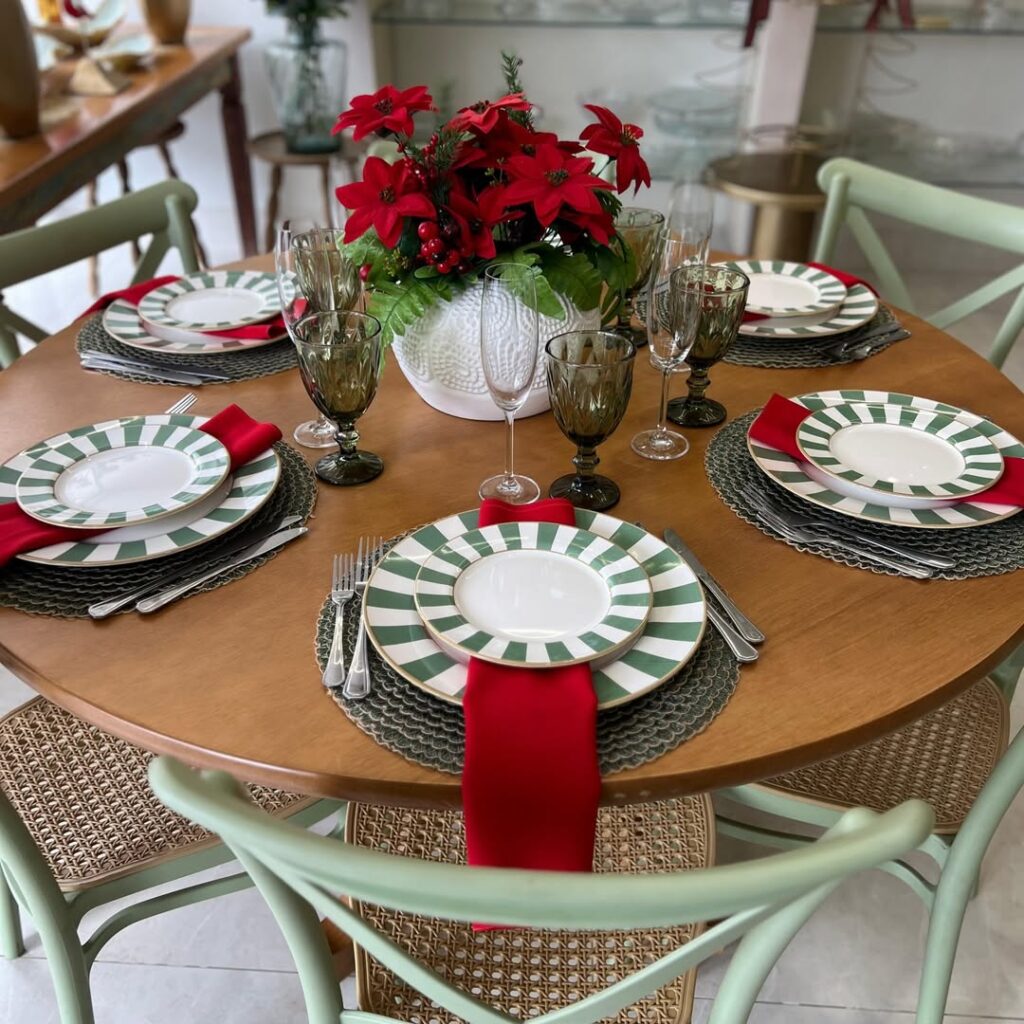 Mesa decorada para o Natal com sousplats, pratos listrados em branco e verde, e guardanapos vermelhos