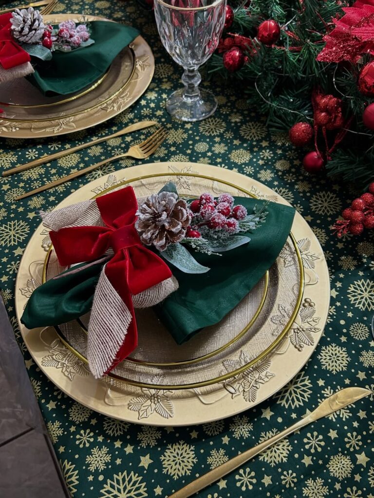 Mesa com sousplat dourado e guardanapo verde com pinha e laço vermelho