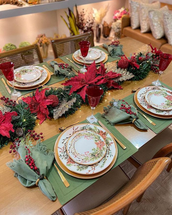Mesa de madeira decorada com jogoas americanos e guardanapos verde, pratos com flores e centro de mesa em vermelho, verde e dourado
