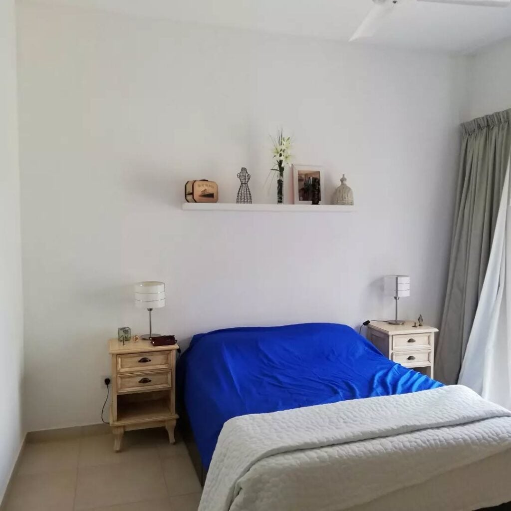 Quarto com parede branca, cama sem cabeceira e prateleira acima