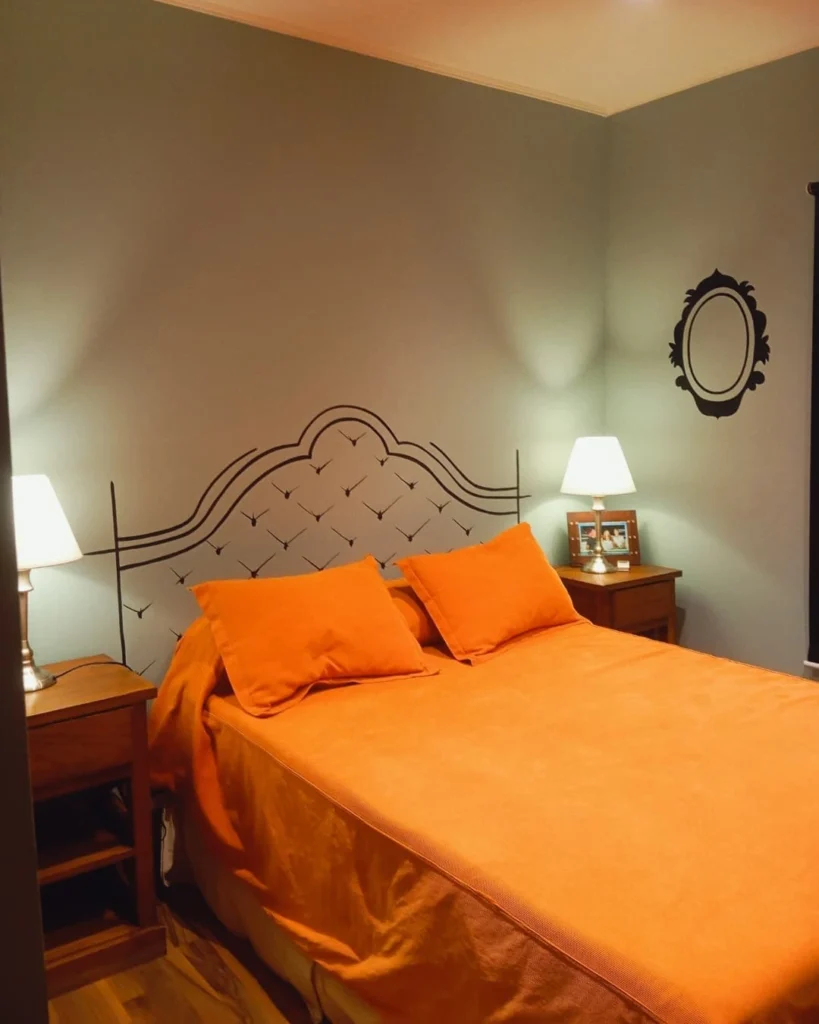 Quarto com roupa de cama laranja e pintura que imita uma cabeceira