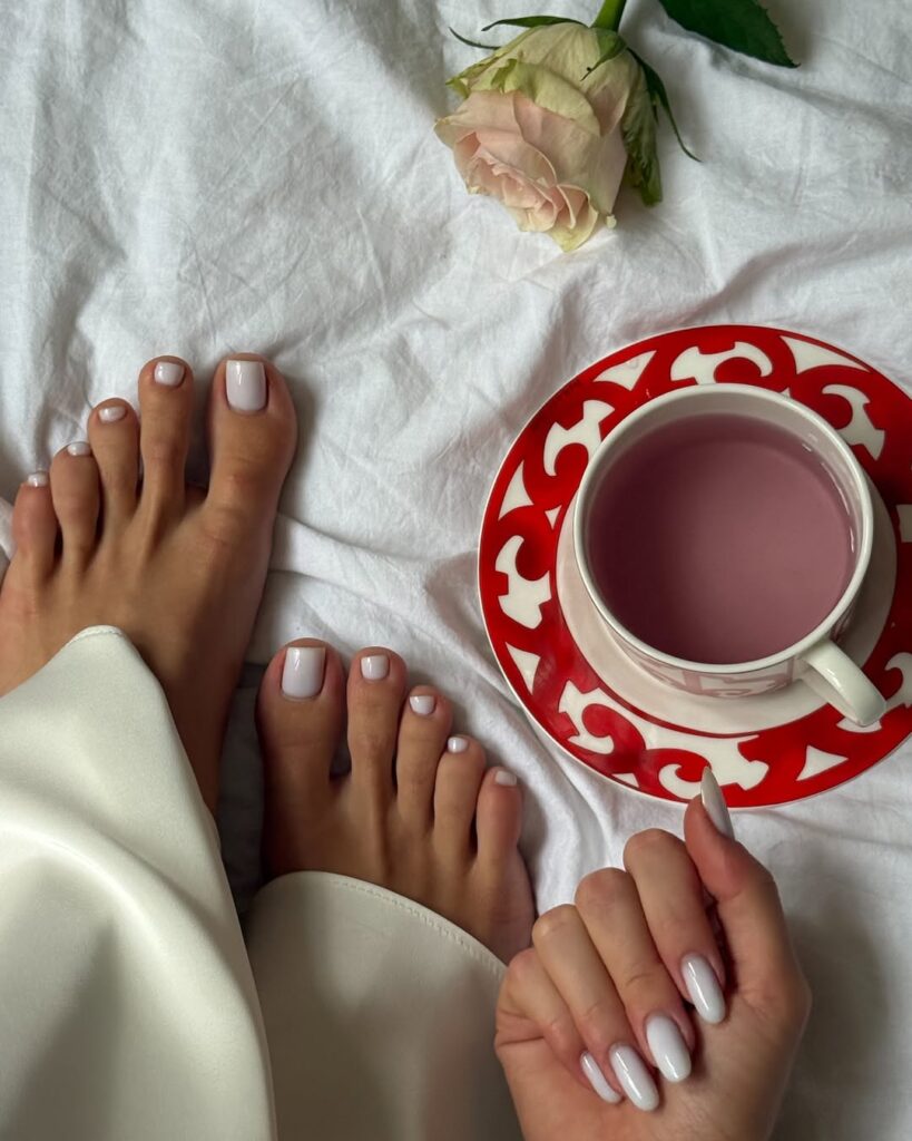 Mulher de pele clara, com unhas dos pés e das mãos pintadas com esmalte branco 