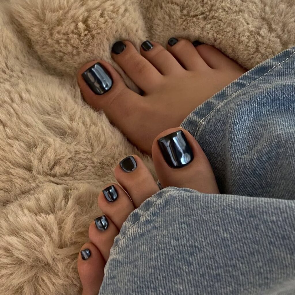 Pés de pele clara, com unha pintada com esmalte preto e acabamento cromado 