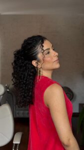 Mulher de pele clara, com vestido vermelho e cabelo cacheado escuro em penteado semipreso