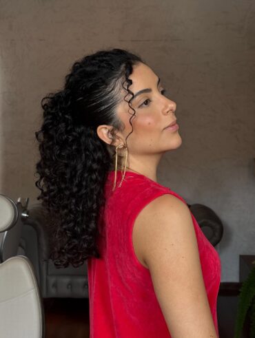 Mulher de pele clara, com vestido vermelho e cabelo cacheado escuro em penteado semipreso