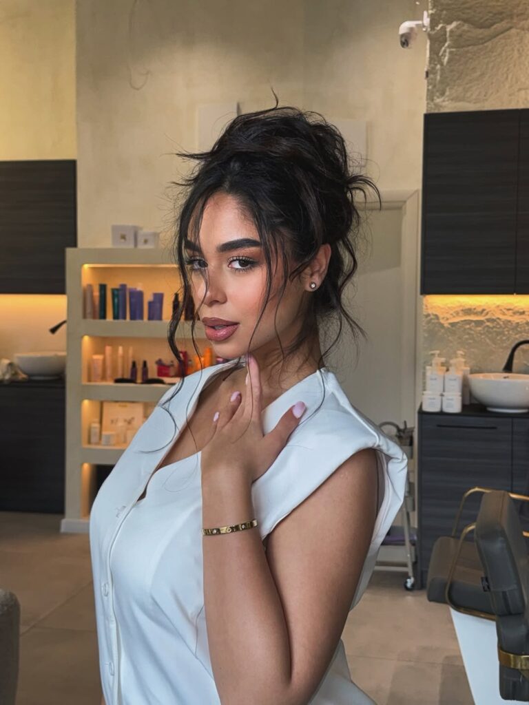 Mulher de pele clara, com blusa branca e cabelo escuro com coque messy 
