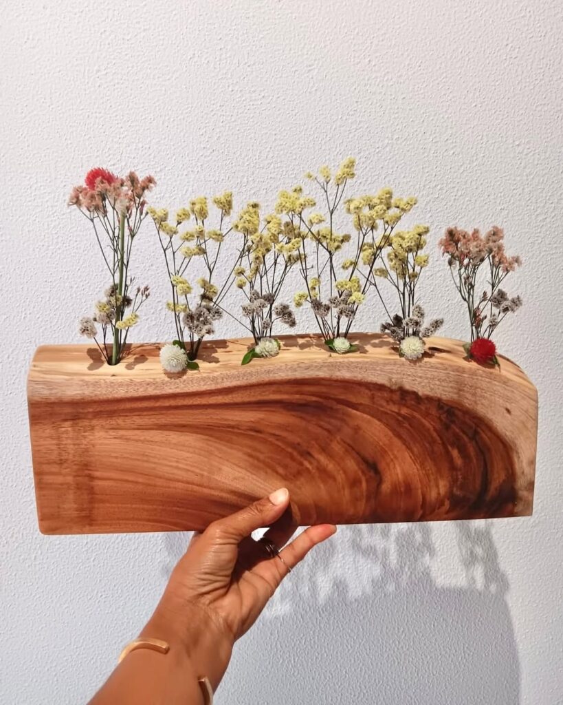 Mão segurando uma floreira de madeira com florzinhas