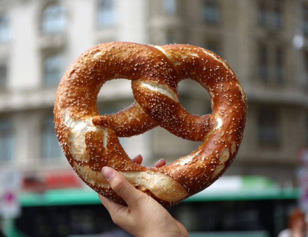 Mão segurando um pretzel grande e douradinho