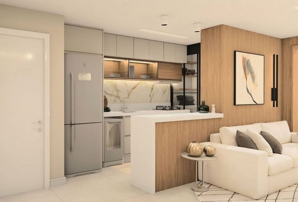 Cozinha com armários e geladeira em tom de cinza com painel amadeirado integrando a sala e sofá branco
