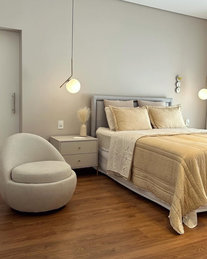 Quarto em tons claros com cabeceira estofada, pendentes e poltrona confortável
