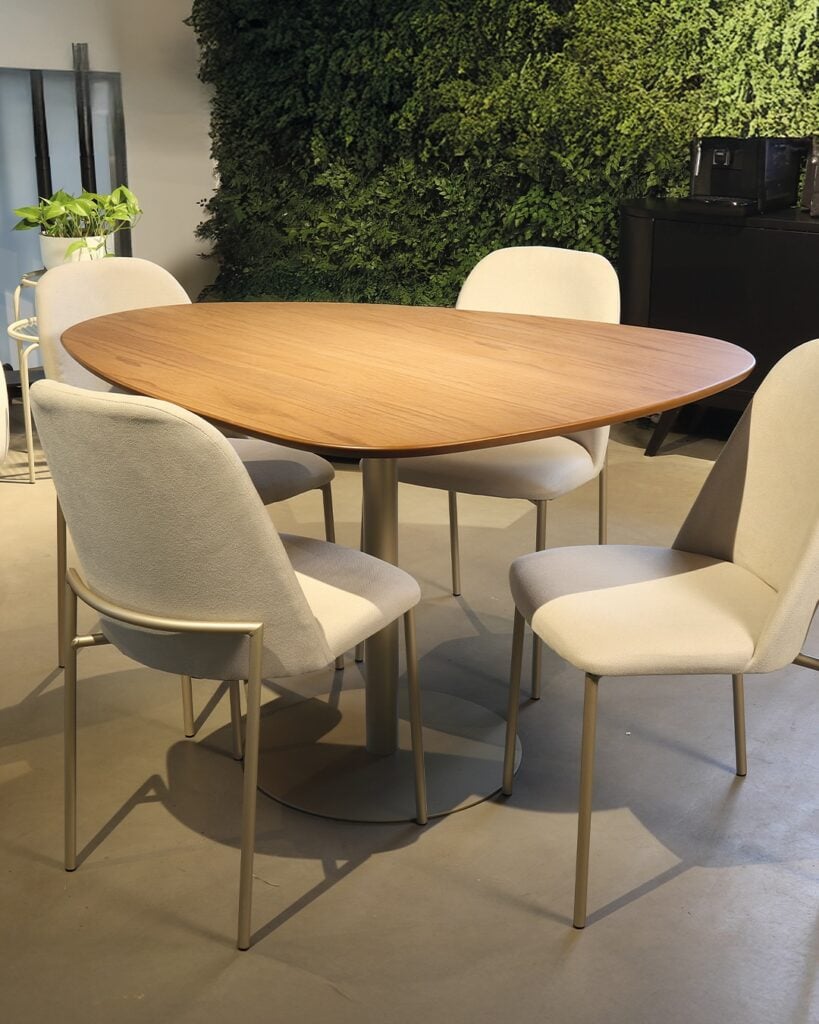 Mesa com design orgânico e cadeiras estofadas claras, com parede verde que é uma das tendências
