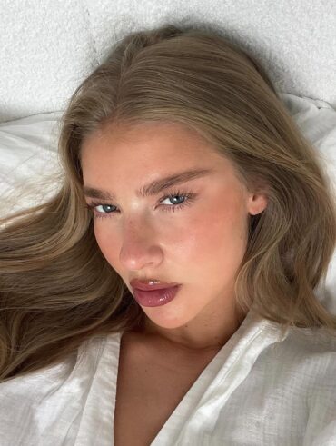Mulher de pele clara, com roupão branco, cabelo claro e lash lifting