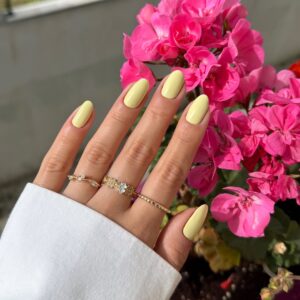 Mão de pele clara, com anéis e unha amendoada amarelo-manteiga