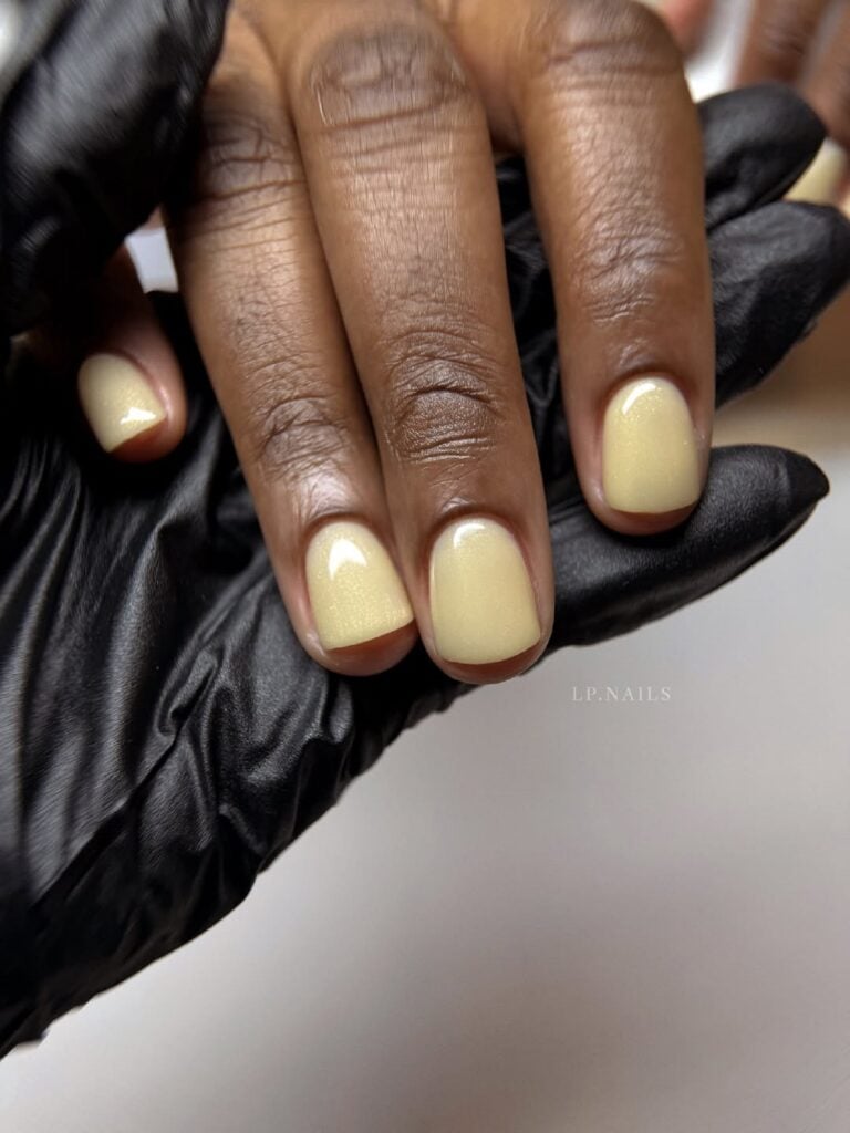 Mão de pele negra com unha tamanho curto e formato quadrado com esmalte amarelo manteiga cintilante