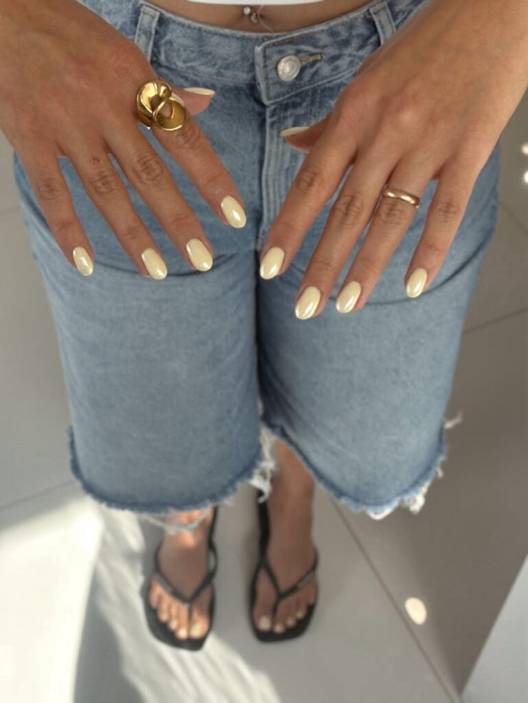 Mão de pele branca com unha tamanho médio e formato amendoado com esmalte amarelo manteiga perolado