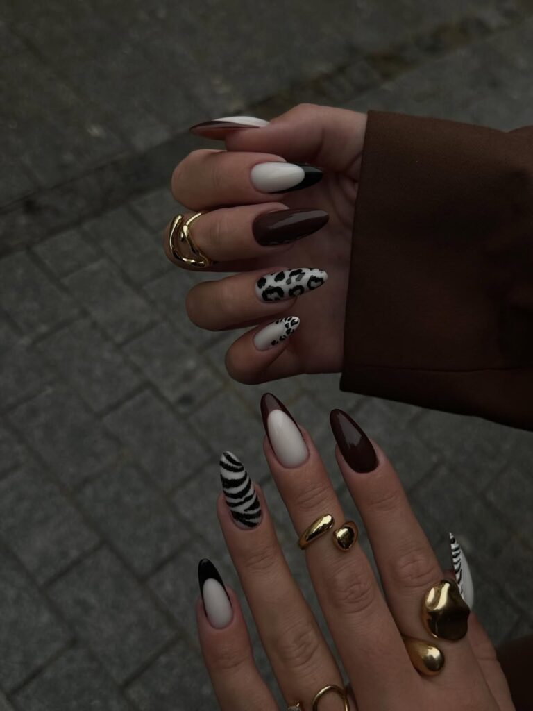 Mãos de pele clara, com anéis em dourado e unha amendoada em tons de marrom e com decoração animal print