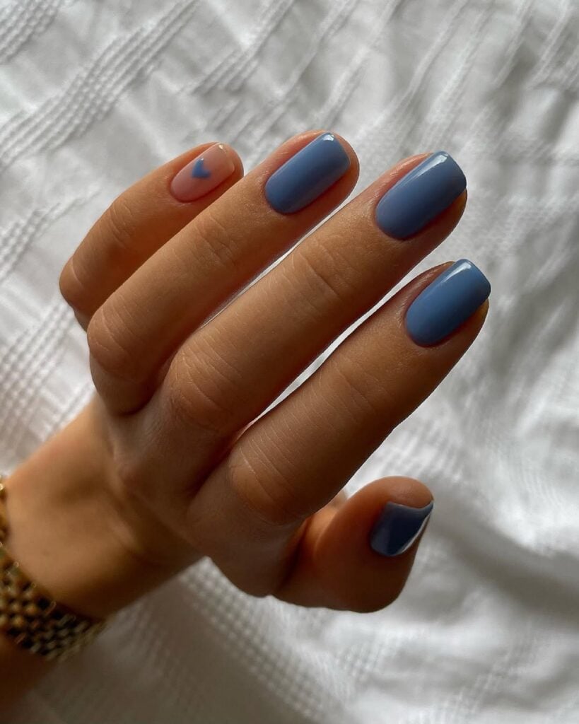 Mão de pele branca com unha tamanho médio e formato quadrado com esmalte azul claro com nail art de coração