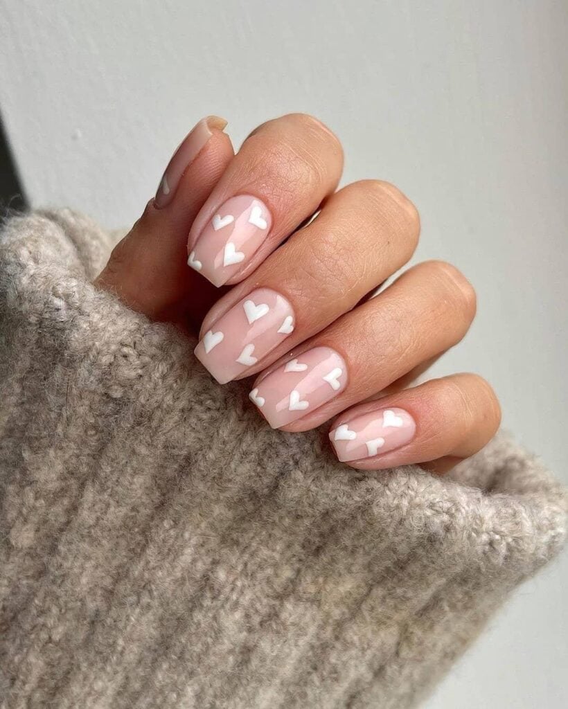 Mão de pele branca com esmalte branco com nail art de coração