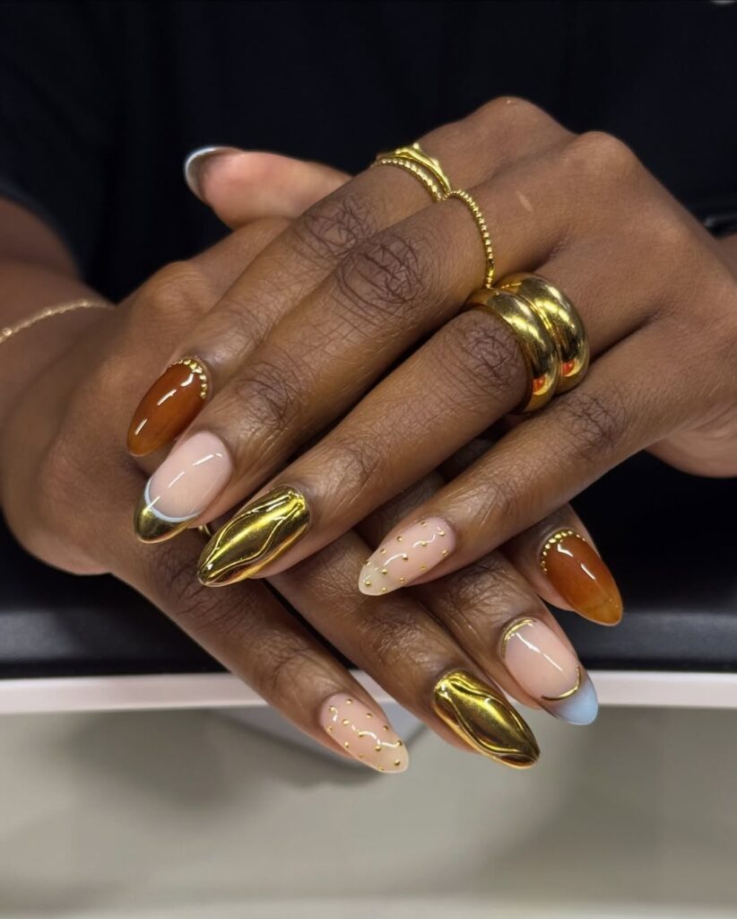 Mãos de pele preta, com anéis em dourado e unha amendoada decorada com dourado 