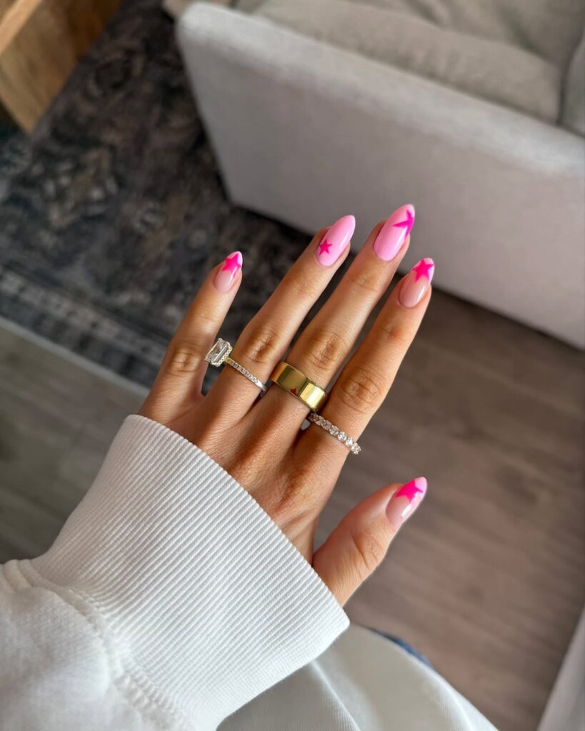 Mão de pele clara, com anéis em prata e unha amendoada rosa-claro com estrelas