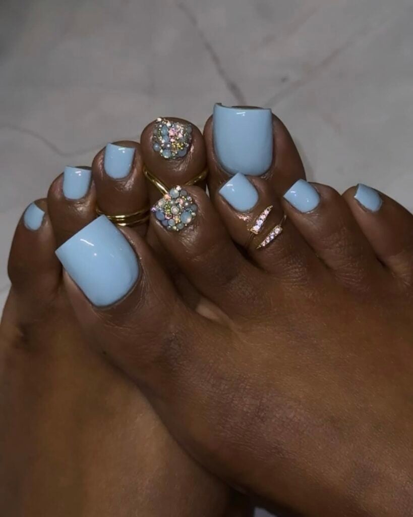 Pés de pele preta, com anéis e unhas dos pés pintadas com esmalte azul-claro de decorada com strass