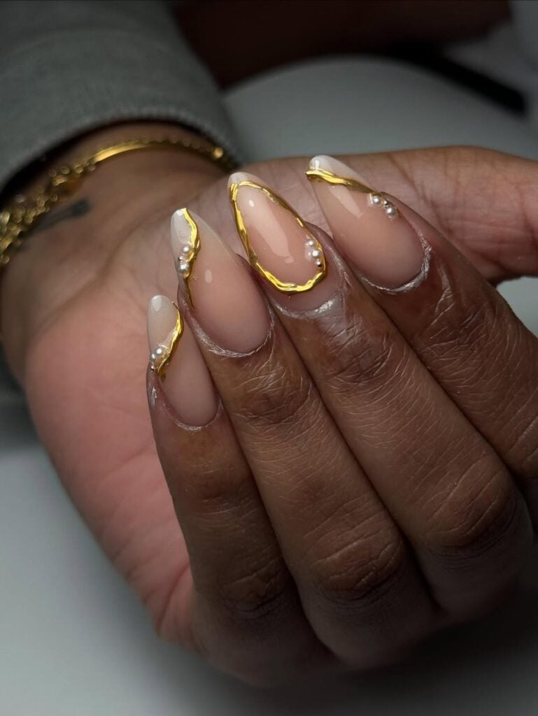 Mão de pele preta com unha amendoada com detalhes em dourado e com pérolas