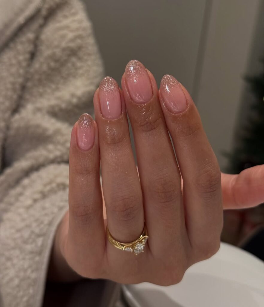 Mão de pele clara, com anel em dourado e unha amendoada neutra com ombré dourado 