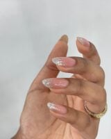 Mão de pele clara, com anel dourado e unha amendoada com ombré com glitter