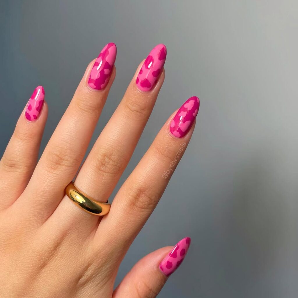 Mão de pele clara, com anel dourado e unha amendoada rosa decorada