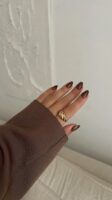 Mão de pele clara, com anel dourado e unha amendoada marrom