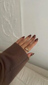 Mão de pele clara, com anel dourado e unha amendoada marrom