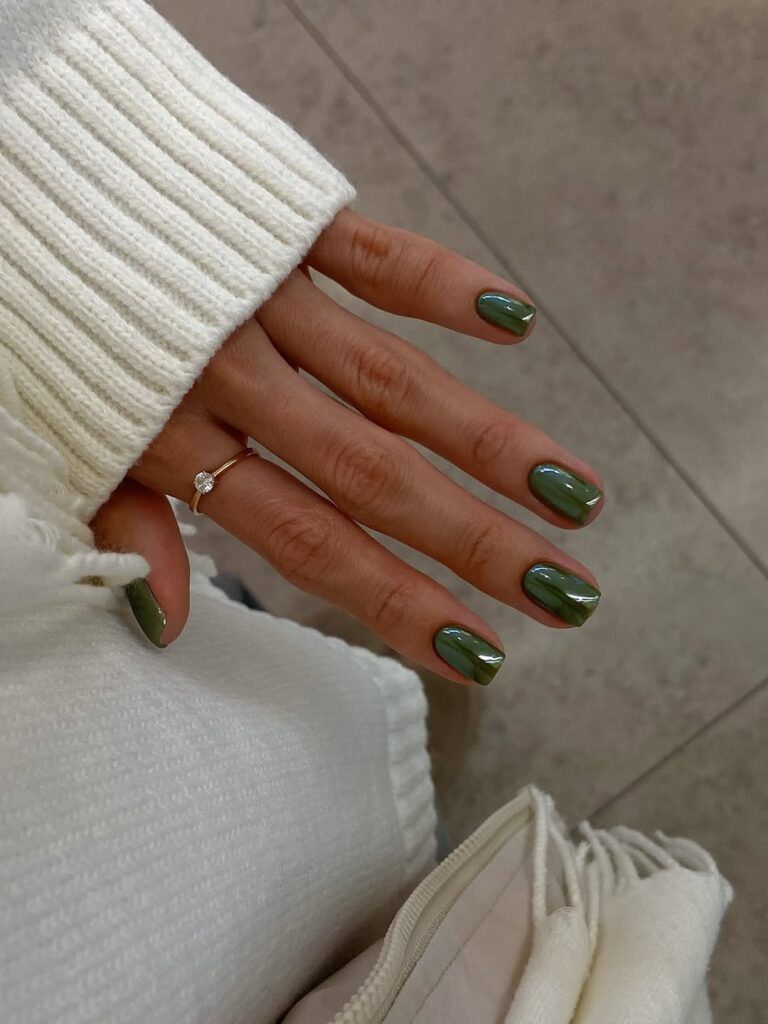 Mão de pele clara, com anel dourado e unha curta e quadrada verde com acabamento cromado