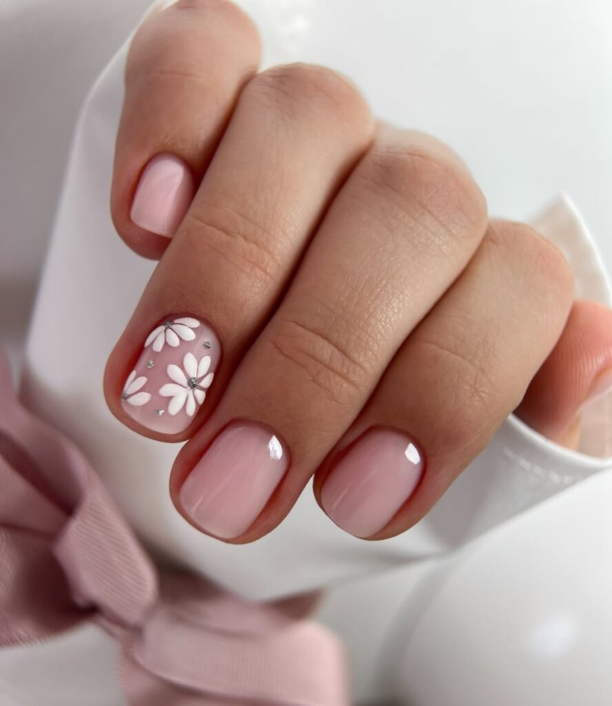 Mão de pele clara, com unha rosa-claro com flores para decorar