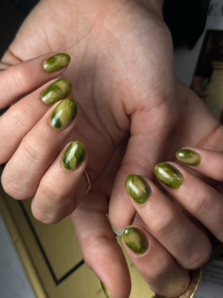 Mãos de pele clara, com unhas curtas em tons de verde e marmorizadas
