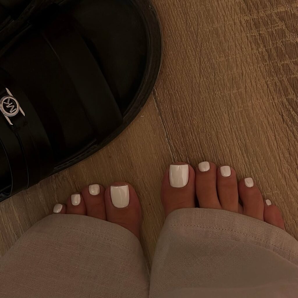 Pés de pele clara, com unhas pintadas com esmalte branco cromado