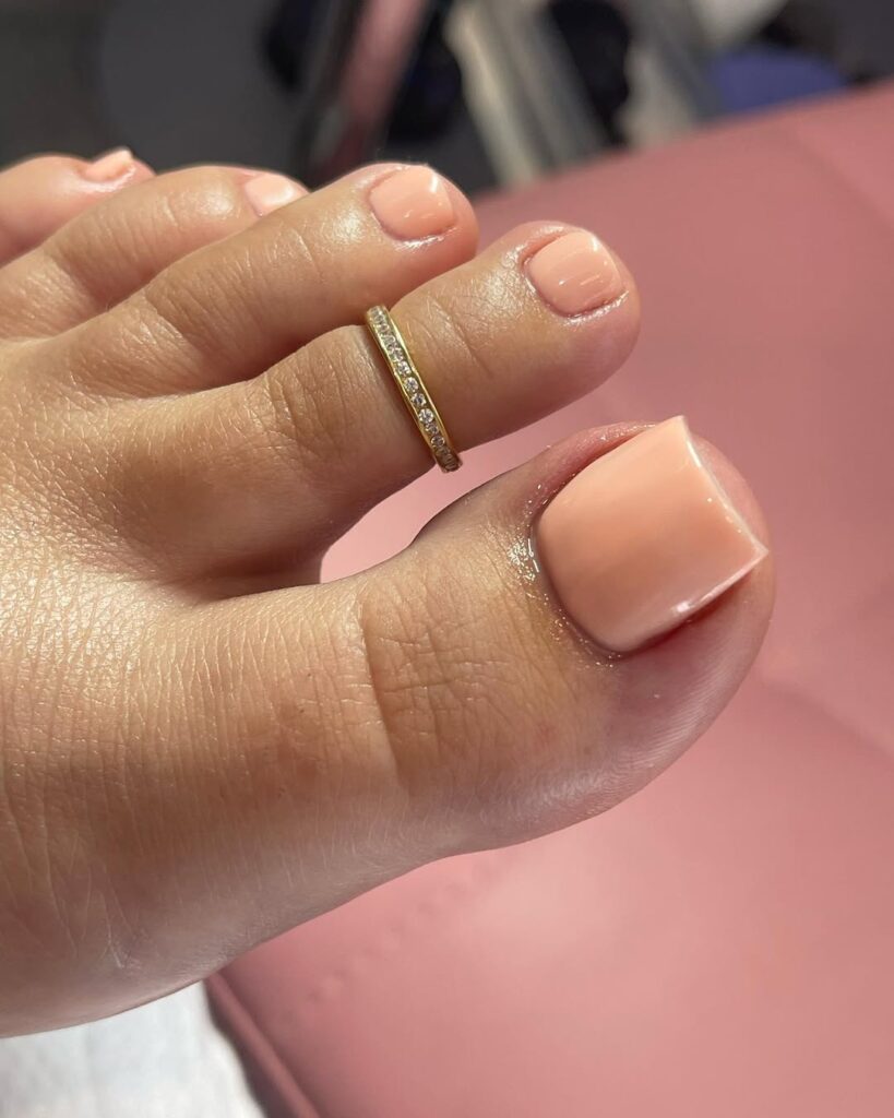 Pé de pele clara, com anel e unhas pêssego 