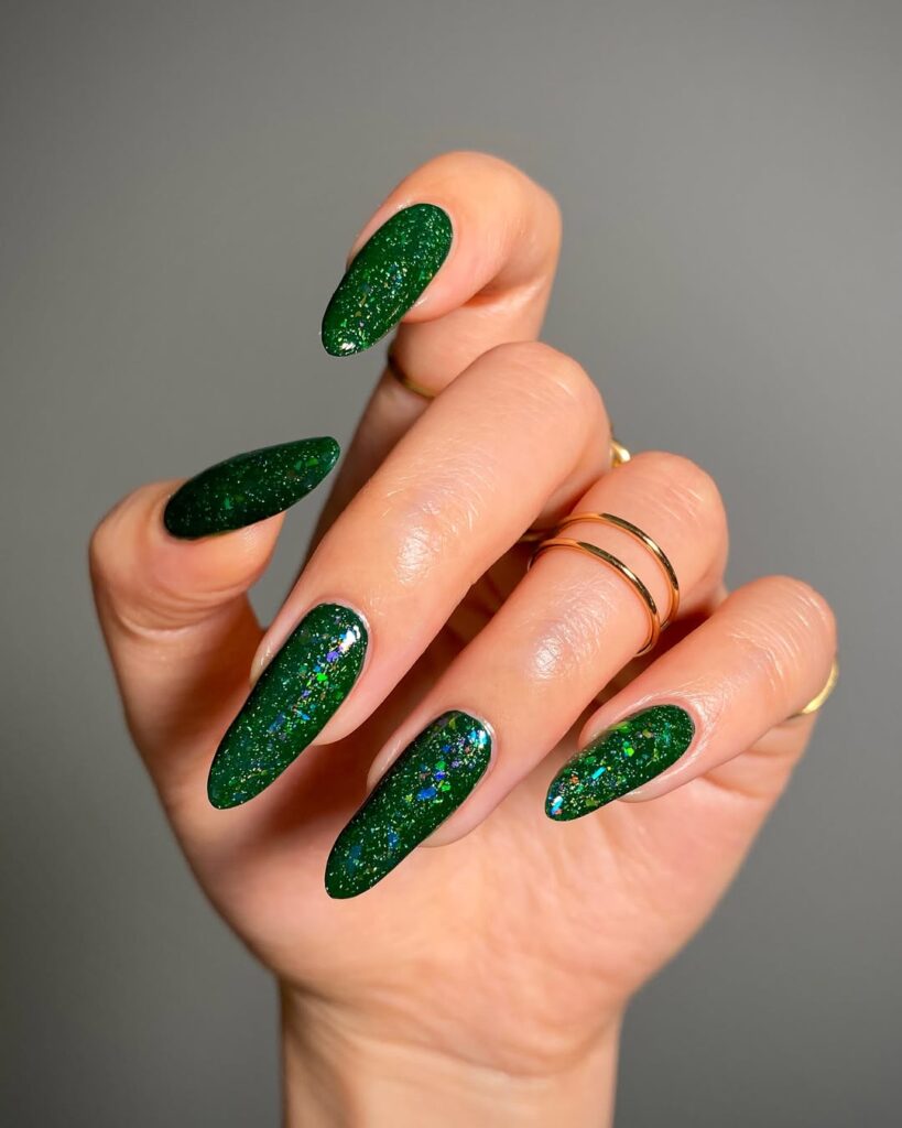 Mão de pele clara, com anéis em dourado e unha amendoada longa verde com brilho
