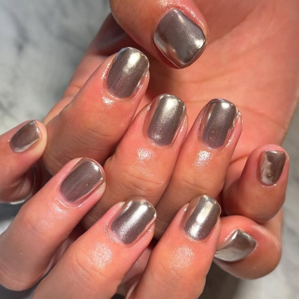 Mãos de pele clara, com unhas curtas pintadas com esmalte prata 