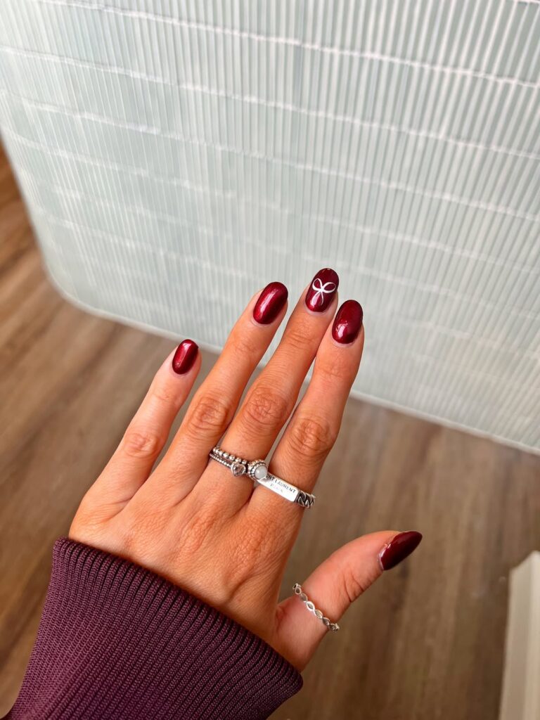 Mão de pele clara, com anéis em prata, unha curta amendoada com esmalte vermelho metalizado com çaõs