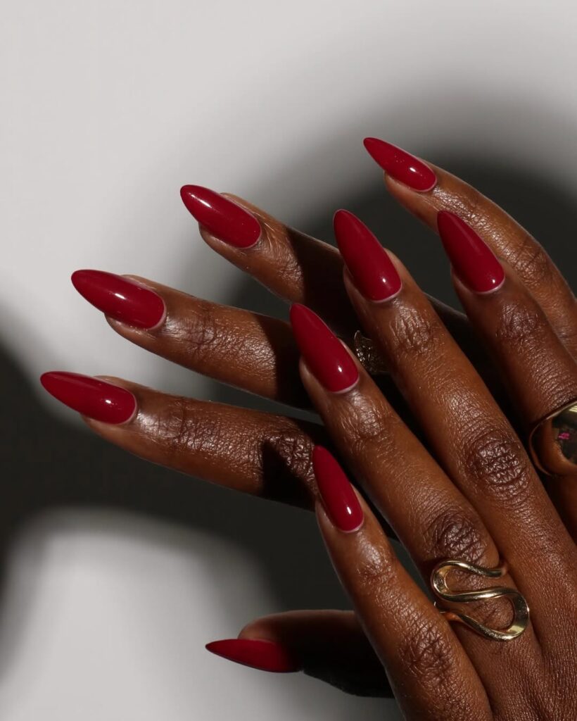 Mãos de pele preta, com anéis e unha amendoada vermelho-escuro