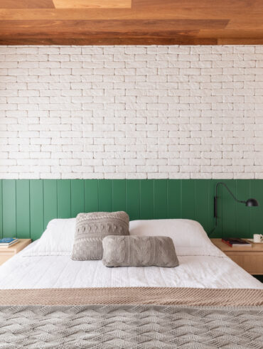 Quarto com parede de tijolinhos brancos, cama com cabeceira em painel verde