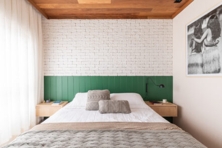 Quarto com parede de tijolinhos brancos, cama com cabeceira em painel verde