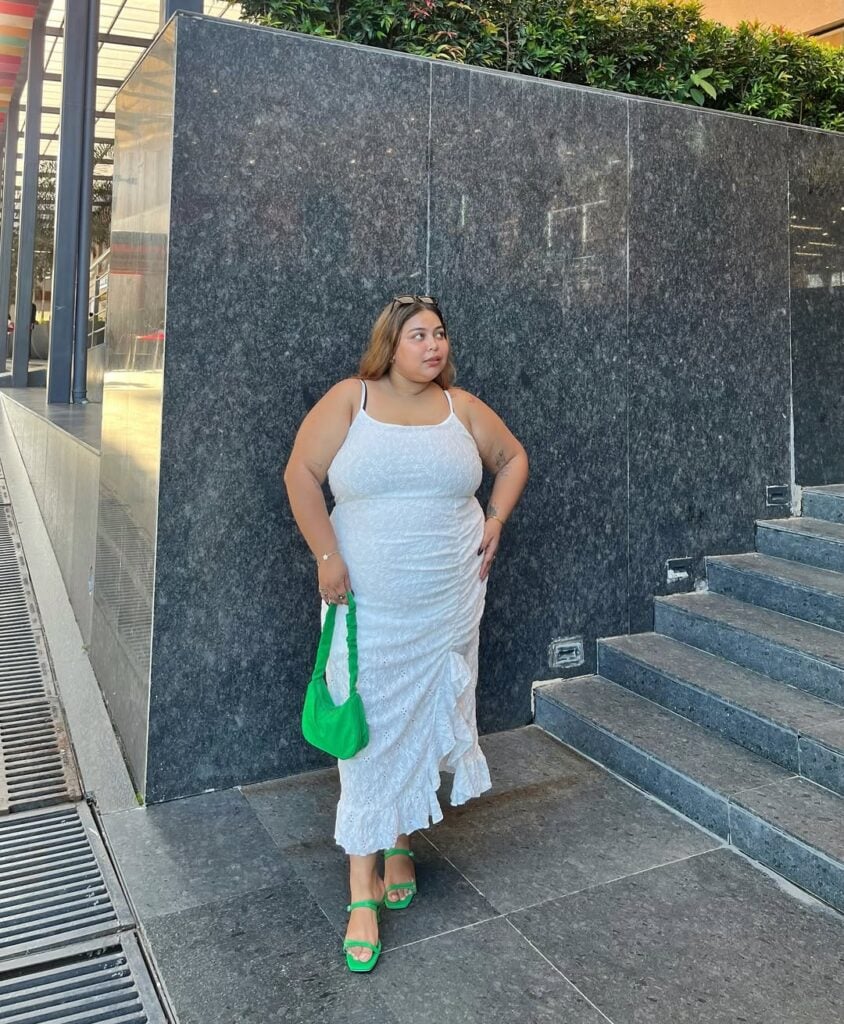 Mulher jovem com vestido midi branco, bolsa e sapato verde e óculos de sol peças da moda para o verão 2026