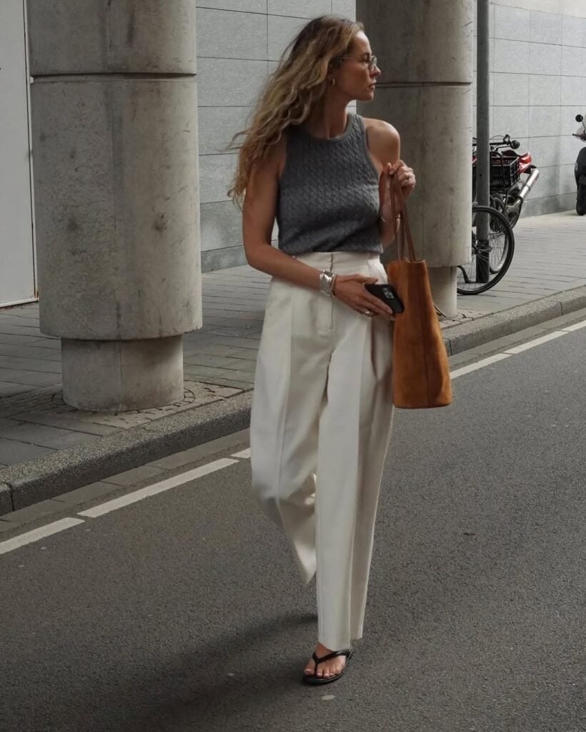 Mulher jovem e magra com regata cinza, calça off-white e chinelo de dedo