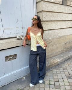 florettenacer usando blusa de alça amarelo-manteiga, calça de alfaiataria cinza e tênis e óculos de sol verde