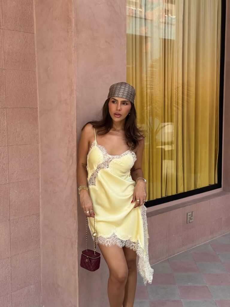 Mulher jovem e magra usando vestido acetinado amarelo, lenço na cabeça e bolsa vermelha