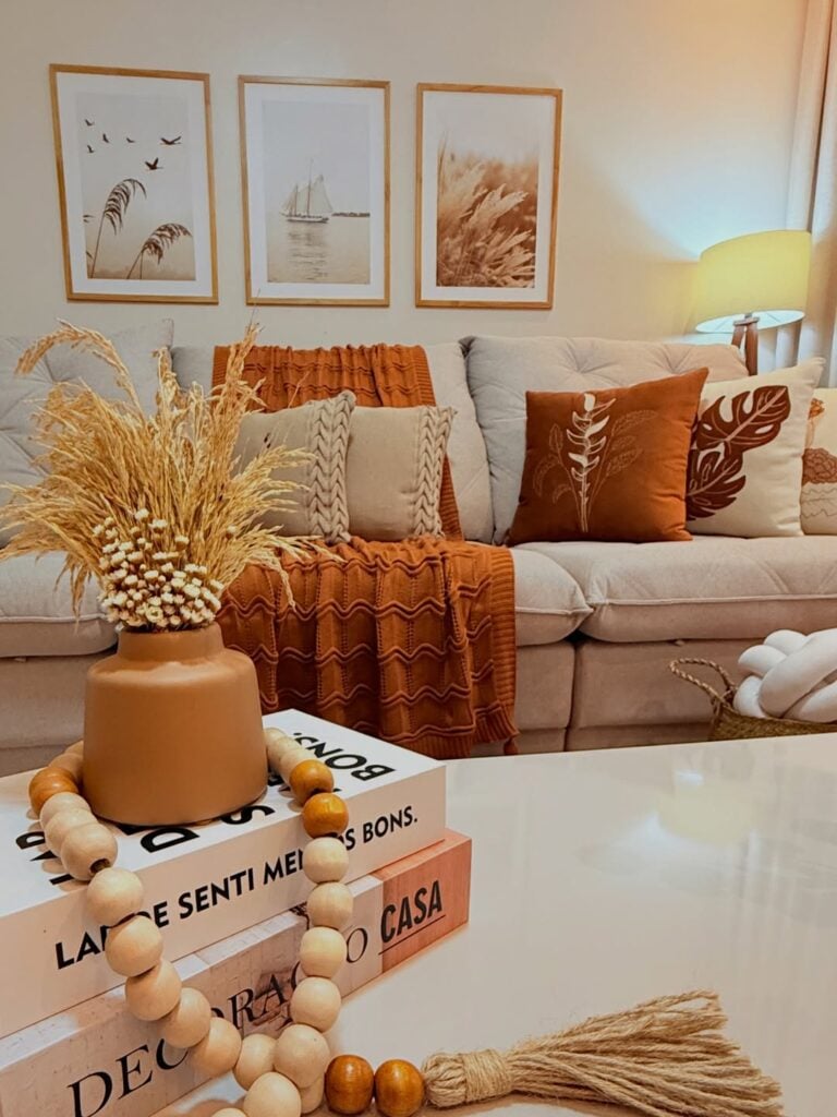 Sala de estar em tons claros e terracota, sofá com almofadas e quadros na parede